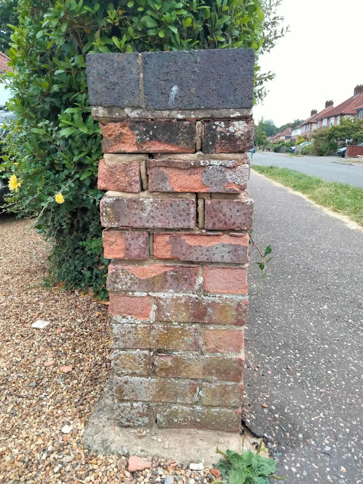 A damaged brick gate pier with missing bricks and a broken top